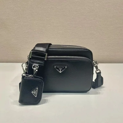 A black leather crossbody camera bag with a detachable zip pouch, on a pale grey surface