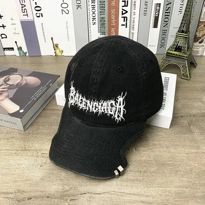 A washed black baseball cap with a spiky embroidered wordmark, resting on a desk beside magazines