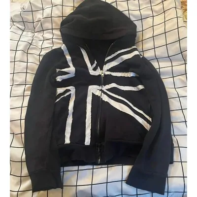 A black zip through hoodie with a large white cross print across the chest, laid on a checked blanket