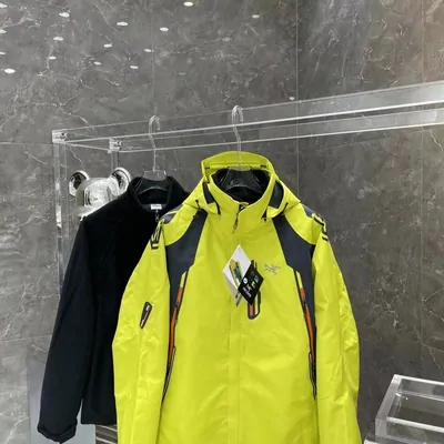 A high visibility yellow technical shell jacket on a hanger, with darker jackets racked behind it